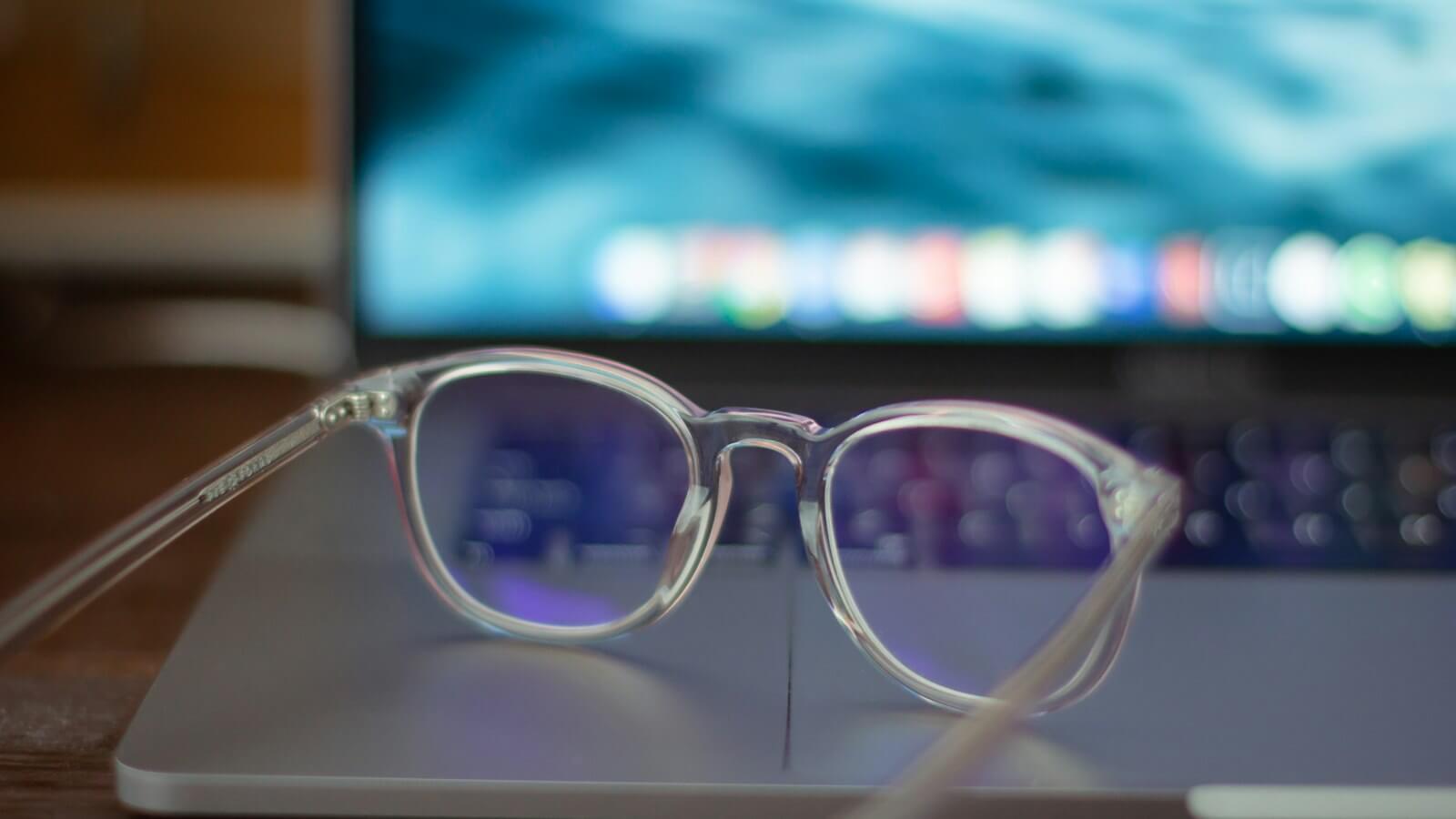 Clear eyeglasses resting on a laptop in front of a glowing screen