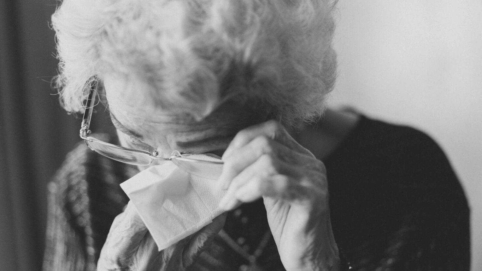 Older woman in glasses wiping her eyes with a tissue