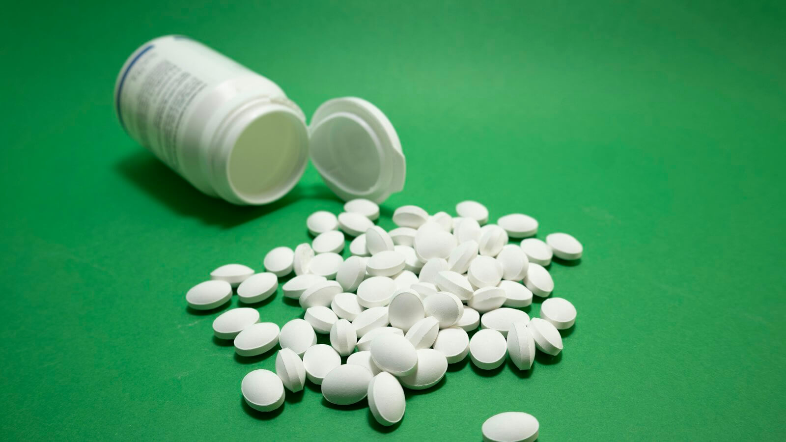 White tablets spilling from an open supplement bottle on a green surface