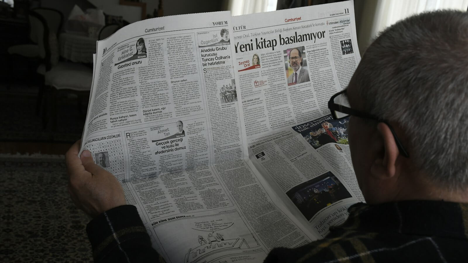 Older man wearing glasses reading a printed newspaper