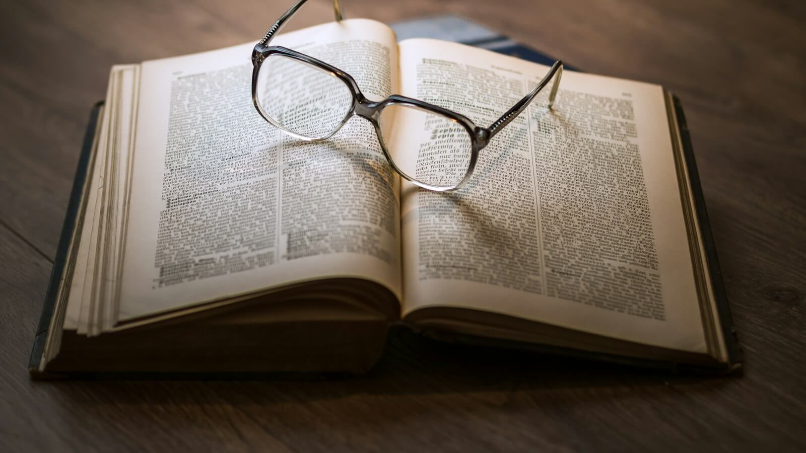 Reading glasses resting on an open book on a wooden table