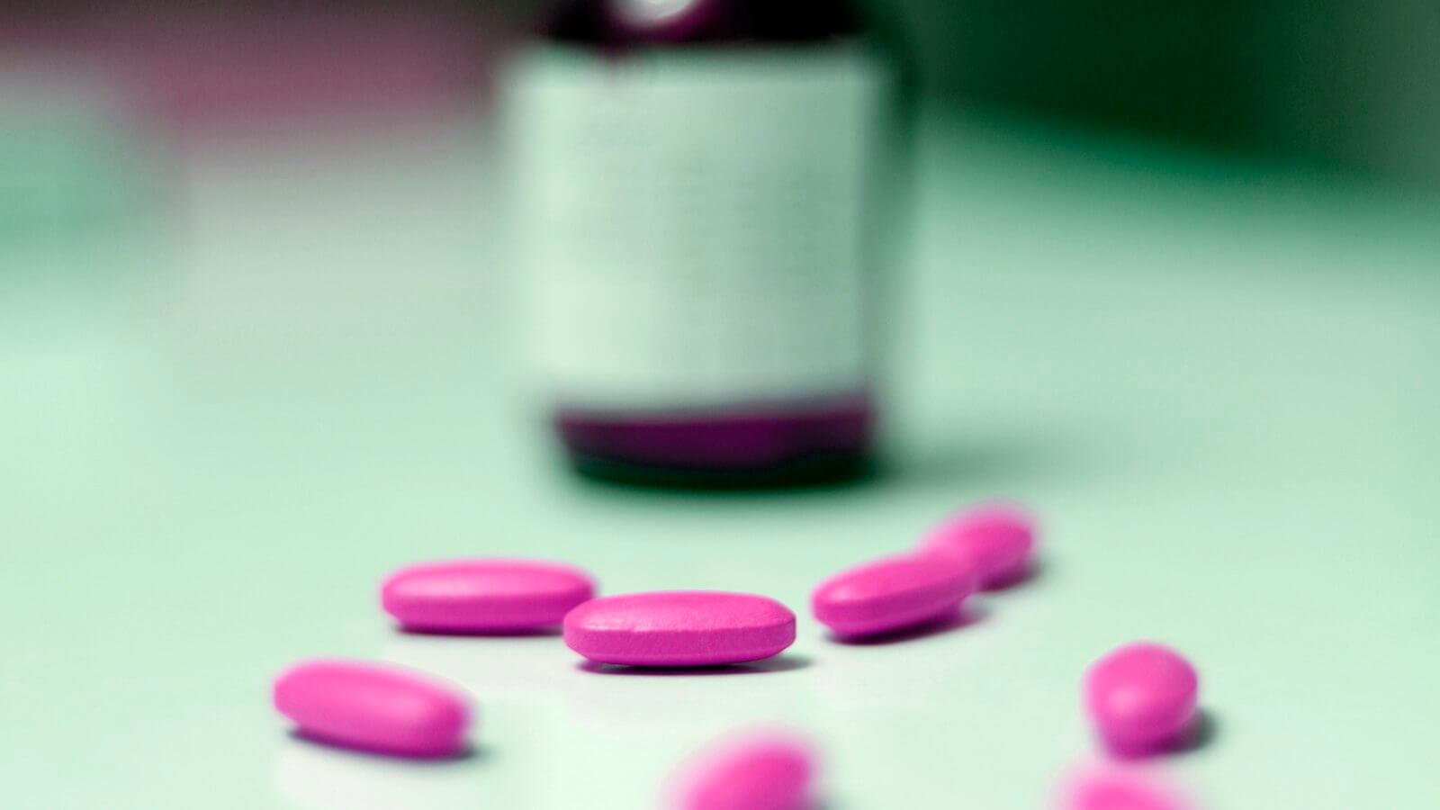 Pink tablets on a table in front of a blurred supplement bottle