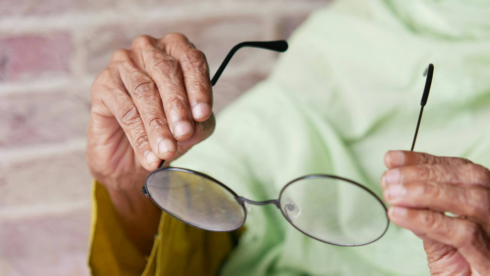 Older woman's hands holding a pair of round reading glasses